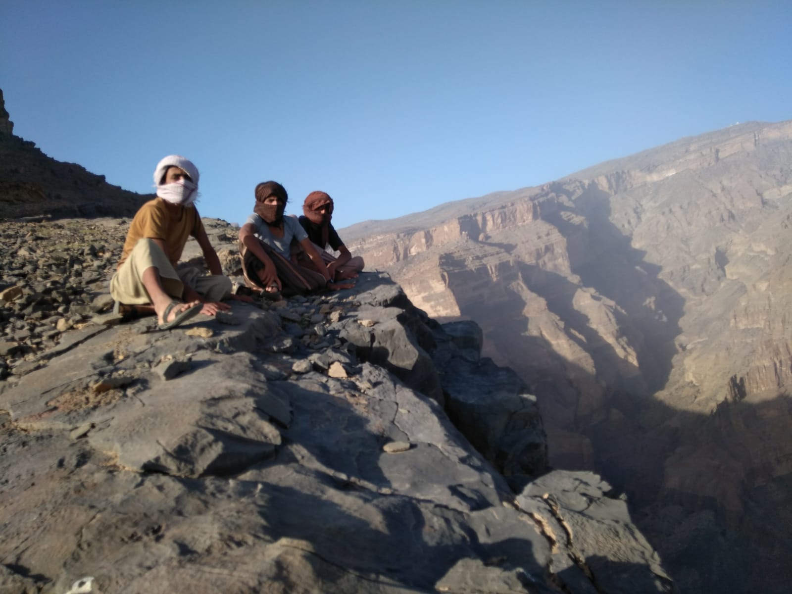 Groupe d'enfants omanais portant le chèche assis au bord du vide sur les hauteur d'un profond canyon.