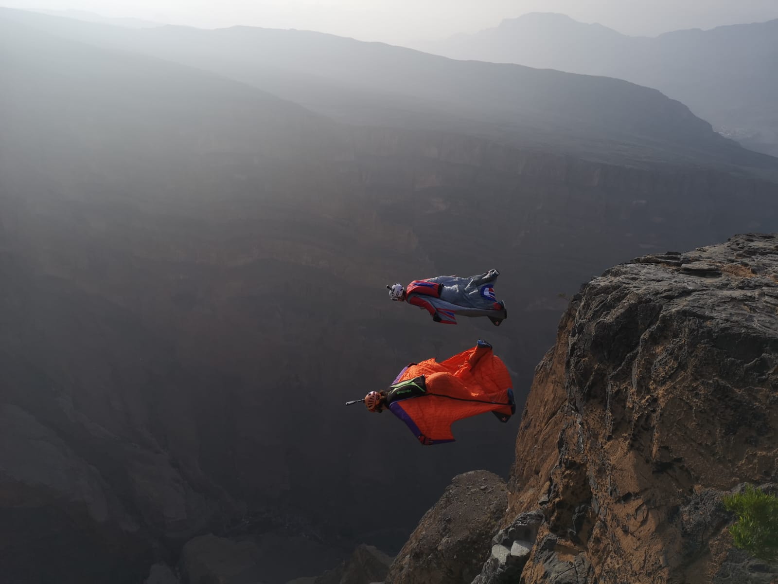 Two base jumpers wearing a wingsuit jump off a cliff during a base jumping expedition in Oman with BASE Spirit.